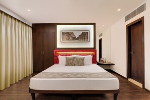 A modern hotel room with a large bed, a red headboard, a framed picture above the bed, and a wooden wardrobe. - (Hubli)