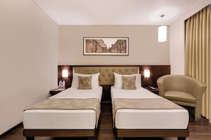 Een hotelkamer met twee bedden, een hoofdbord, nachtkastjes, een lamp, een stoel en een ingelijst schilderij aan de muur.