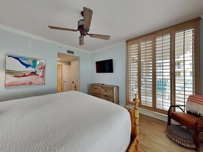 Ein Schlafzimmer mit einem großen Bett, einem Deckenventilator, einem Fernseher und einer Schiebetür zu einem Balkon.