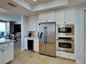 A modern kitchen with white cabinetry, a stainless steel refrigerator, a microwave, and an oven. - Indigo East 601 4 Bedroom Corner Unit w/ Large Balcony, Updated & Owner Managed (Pensacola)