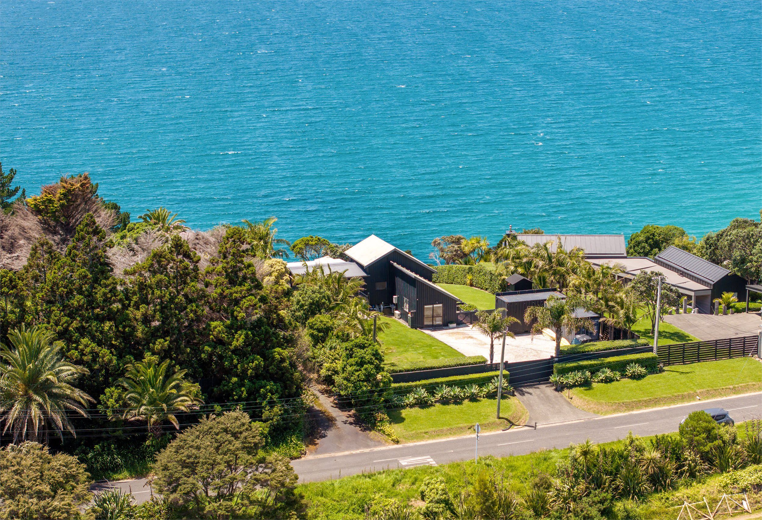 A coastal property with a large house, a swimming pool, and a road leading to the sea.