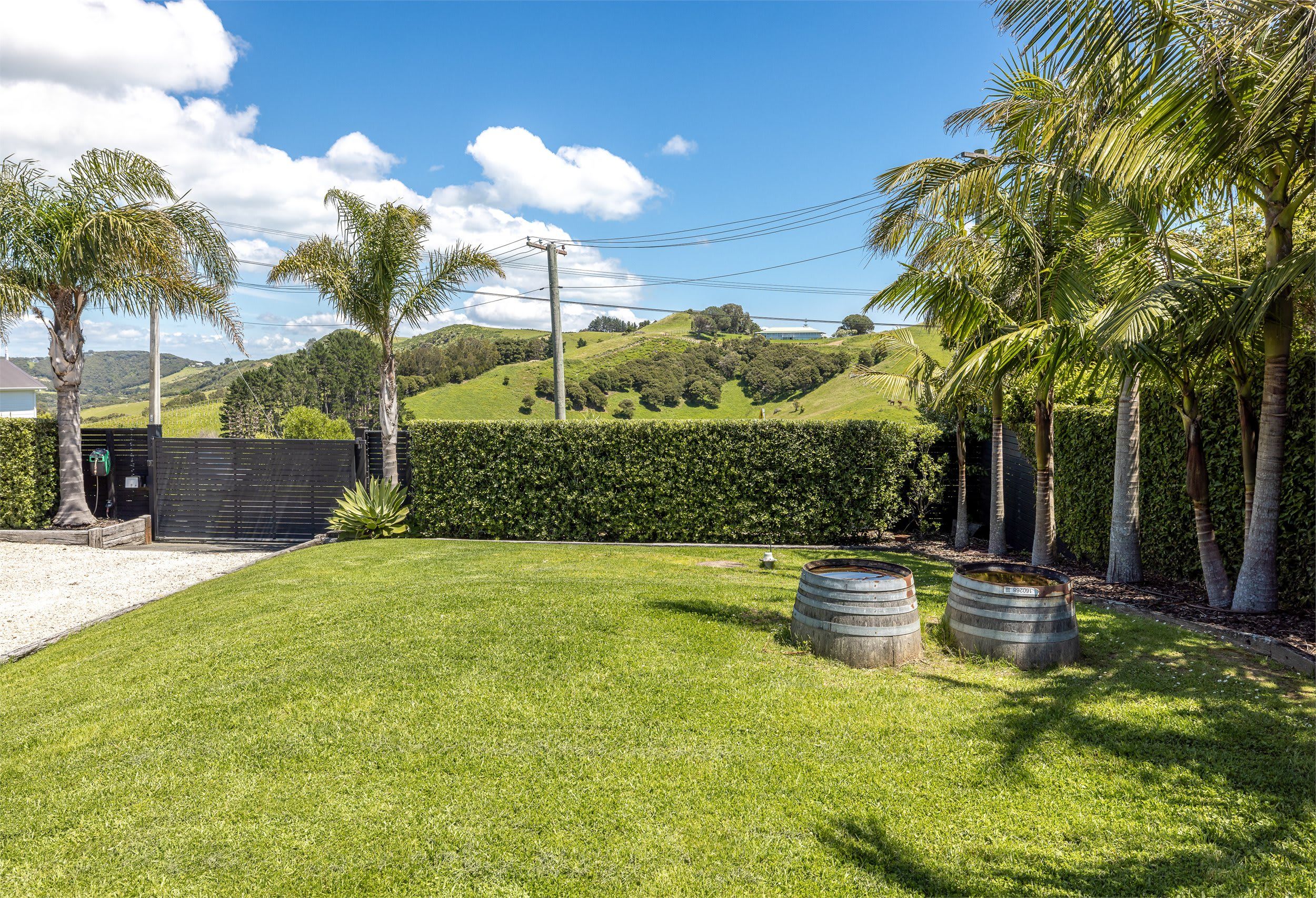 A well-maintained grassy lawn with a hedge, a metal barrel, and a black fence.