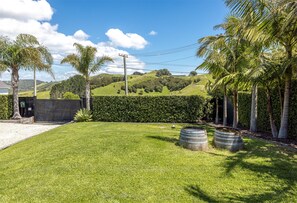 A well-maintained grassy lawn with a hedge, a metal barrel, and a black fence. - Sea Views & Space to Play (Waiheke Island)
