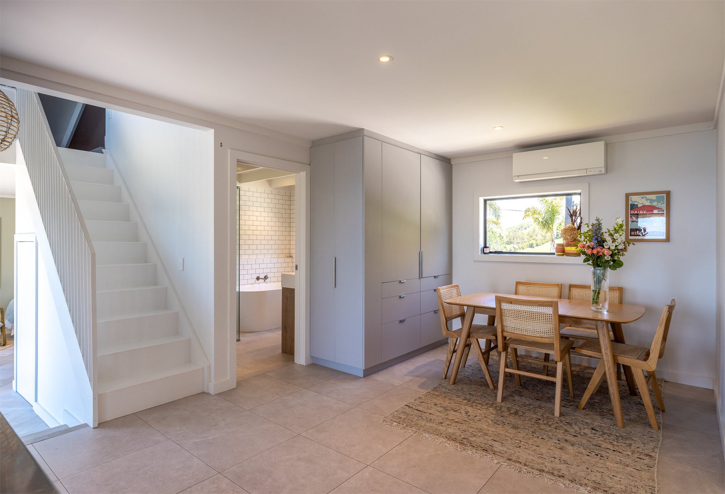 A modern kitchen with white cabinets, a dining area with wooden chairs, and a staircase leading to another level.