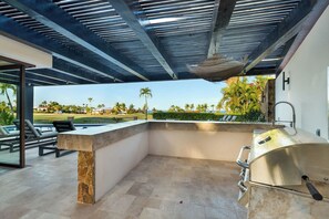 An outdoor kitchen area with a stone countertop, a grill, and a view of a landscaped property. - Luxury Palmilla Golf 4BR Villa w/ Pool & Jacuzzi (San José del Cabo)
