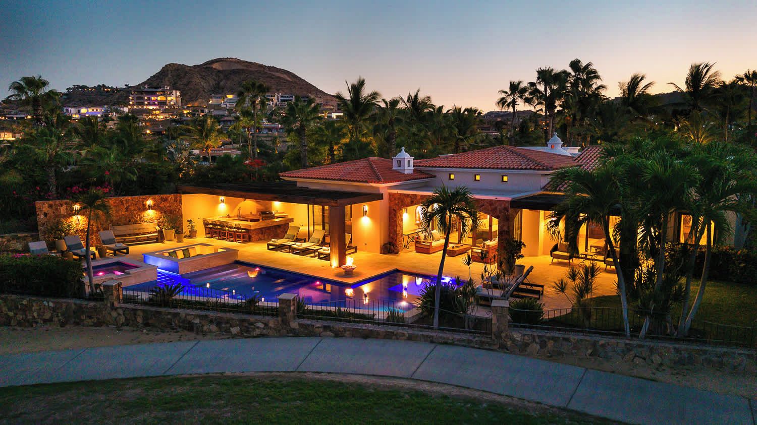 A large house with a swimming pool, outdoor seating, and a view of a hill.