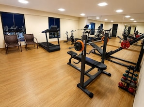 A gym with cardio equipment, weightlifting stations, and a city view through large windows. - CJC Short Stay Paradise (Natal)