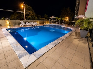 A swimming pool with lounge chairs and umbrellas, surrounded by a tiled deck and potted plants. - CJC Short Stay Paradise (Natal)