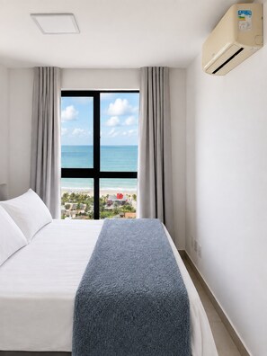 A hotel room with a bed, a window with a view of the beach, and an air conditioning unit. - CJC Short Stay Paradise (Natal)