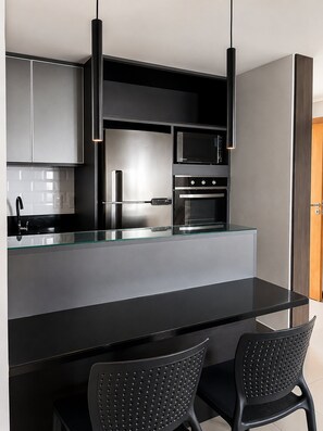 A modern kitchen with a black countertop, stainless steel appliances, and black chairs. - CJC Short Stay Paradise (Natal)