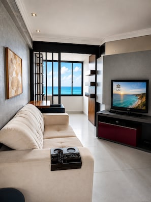 A modern living room with a sofa, a television, and a view of the ocean. - CJC Short Stay Paradise (Natal)