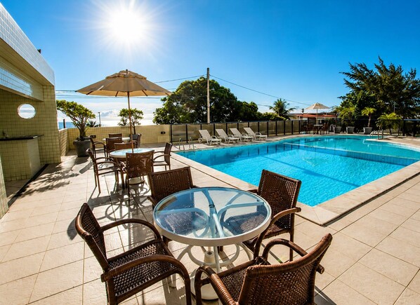 A swimming pool with lounge chairs and a table, surrounded by a tiled patio area. - CJC Short Stay Paradise (Natal)
