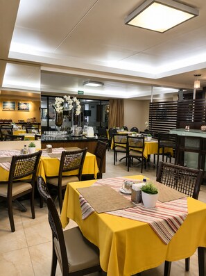 A restaurant with yellow tablecloths, wicker chairs, and a modern interior design. - CJC Short Stay Paradise (Natal)