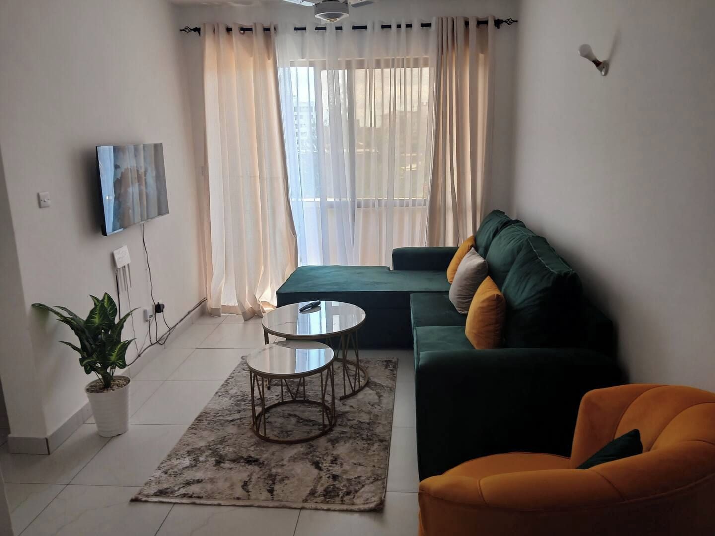 Ein modernes Wohnzimmer mit einem grünen Sofa, einem orangefarbenen Sessel, einem kleinen runden Tisch und einer Topfpflanze.