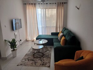 A modern living room with a green sofa, an orange armchair, a small round table, and a potted plant. - Fantastic 1-bedroom apartment in welcoming Mombasa for your stay (Mombasa)