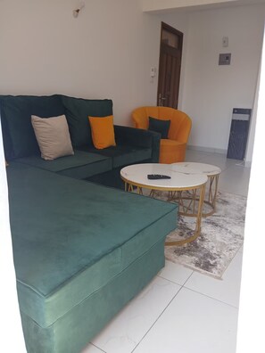 A living room with a green sofa, an orange armchair, and a round coffee table. - Fantastic 1-bedroom apartment in welcoming Mombasa for your stay (Mombasa)