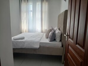 A bedroom with a bed, curtains, and a wooden door. - Fantastic 1-bedroom apartment in welcoming Mombasa for your stay (Mombasa)