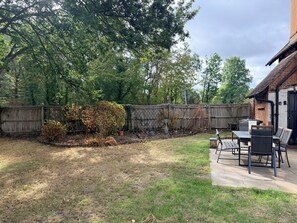 A backyard with a wooden fence, a patio table with chairs, and a brick building. - Hampshire Cottage in Hartley Wintney (Hartley Wintney)