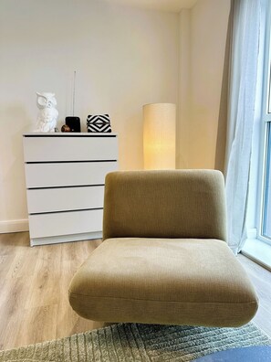 A modern living room with a sofa, a white dresser with decorative items, a tall floor lamp, and a window with curtains. - 2BR Apartment with City Views and Parking (Leeds)