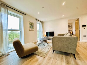 A modern living room with a sofa, a television, and a window with curtains. - 2BR Apartment with City Views and Parking (Leeds)