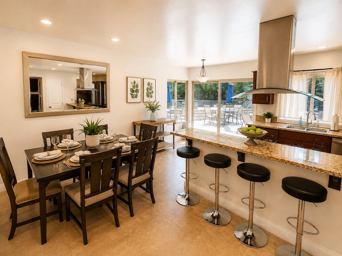 Una cocina moderna con comedor, taburetes de bar y un amplio ventanal con vistas al exterior.