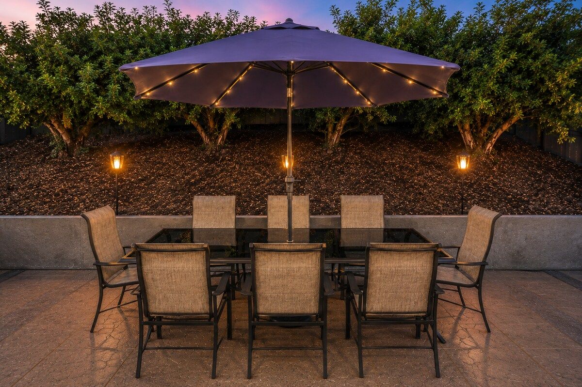 Un patio al aire libre con mesa y sillas, un paraguas grande y luces decorativas.