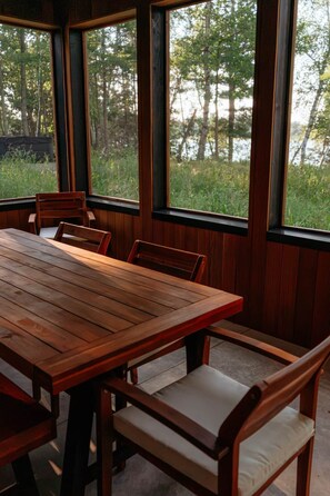 A wooden dining table with chairs, large windows, and a view of trees and a body of water. - NEW | Luxury Lakefront | Hot Tub, Beach & fishing (Backus)