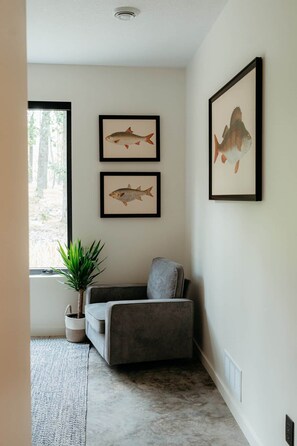 A room with a grey sofa, a potted plant, and two framed fish illustrations on the wall. - NEW | Luxury Lakefront | Hot Tub, Beach & fishing (Backus)