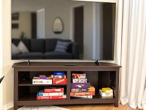 A flat-screen TV on a wooden stand with a shelf below displaying various board games. - Four Kings and Four Baths, Your Retreat by the Strip (Branson)