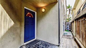 A narrow alleyway with a blue door, a small step leading to a tiled entrance, and a wooden fence on one side.