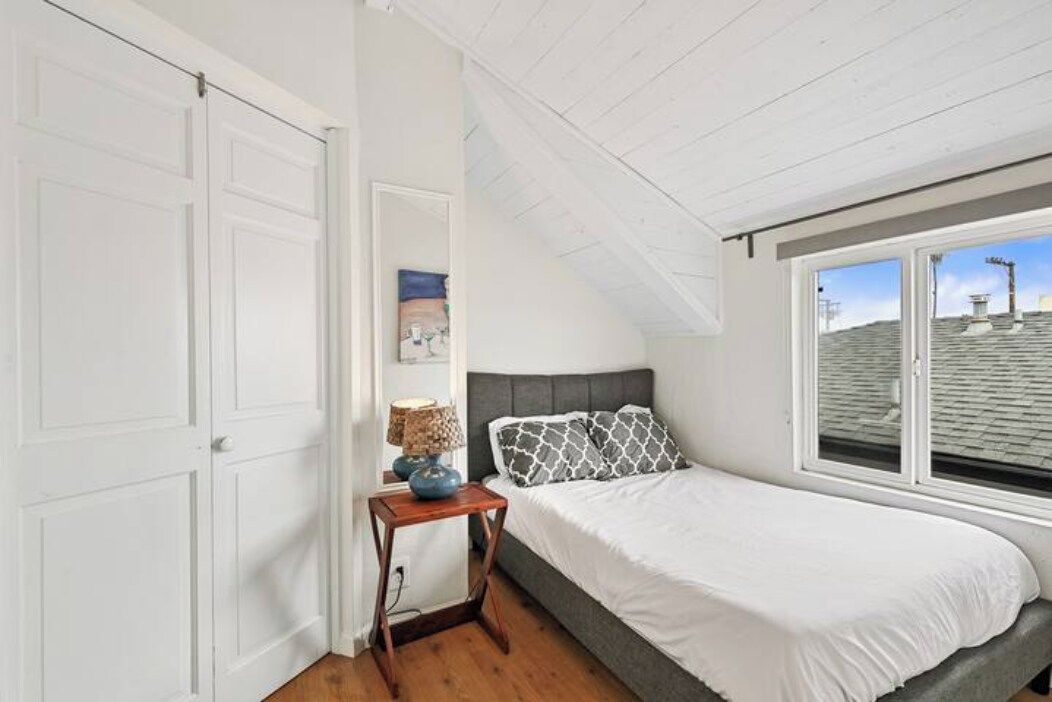 A bedroom with a bed, a nightstand, a window, and a door.