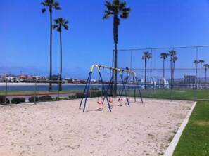 A sandy playground with swings and palm trees in the background. - MB! 6BR Beachhouse- 4 parking spaces Sleeps 20+ (San Diego)