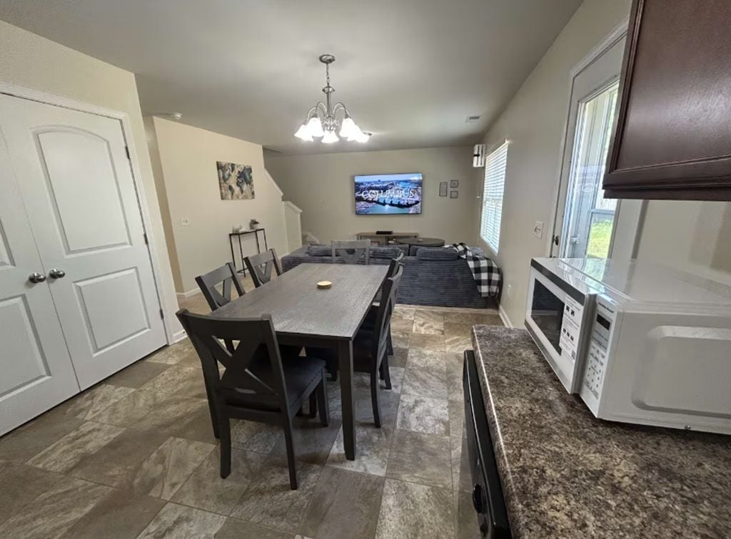 A dining area with a table and chairs, a kitchen with a microwave, and a television on the wall.