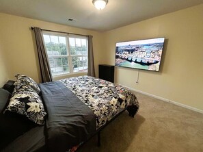 Ein Schlafzimmer mit Bett, Fenster, Fernseher und Blick auf eine Stadtansicht.