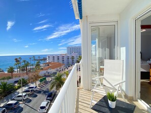Ein Balkon mit Blick auf das Meer, geparkte Autos und ein Gebäude im Hintergrund.