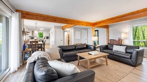 A spacious living area with a wooden ceiling, a central coffee table, and two sofas. - The Beach House | 6BR • Hot Tub • Steps to Lake! (South Haven)