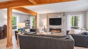 A modern living room with a stone fireplace, leather sofas, and a flat-screen TV. - The Beach House | 6BR • Hot Tub • Steps to Lake! (South Haven)