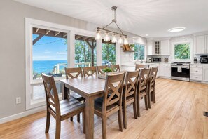 Een ruime keuken met een grote eettafel, houten stoelen en uitzicht op de oceaan.