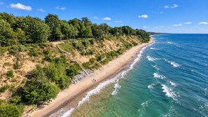 A beach with a wooden walkway leading to the shore, surrounded by dense greenery and a clear blue sky. - The Beach House | 6BR • Hot Tub • Steps to Lake! (South Haven)
