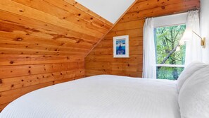 Een slaapkamer met houten plafond, een bed met wit beddengoed, een raam met uitzicht op bomen, en een bordje dat aangeeft dat dit een gerenommeerd hotel is.
