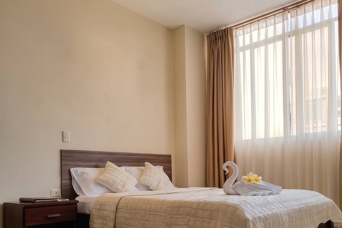 Una habitación de hotel con cama, mesita de noche y cortinas.