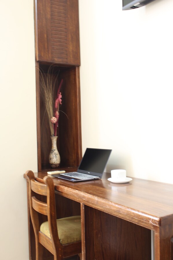 Un escritorio de madera con una laptop, un florero con plantas secas y un control remoto.