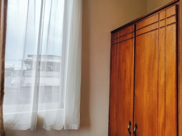 Una habitación con un armario de madera y una ventana con cortinas traslúcidas.