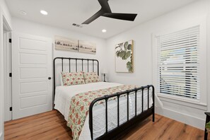 Un dormitorio con cama, ventilador de techo, ventana con persianas y una puerta.