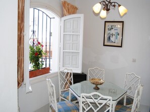 Ein Zimmer mit einer weißen Tür, einem Tisch mit Stühlen, einem Fenster mit Blick auf einen Balkon und einer Wandleuchte.