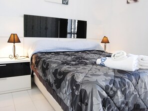 Ein Hotelzimmer mit einem Bett, zwei Nachttischlampen und einem ordentlich gefalteten Handtuch auf dem Bett.