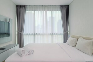 Ein Hotelzimmer mit Bett, Flachbildfernseher, Nachttisch und einem Fenster mit Vorhängen.