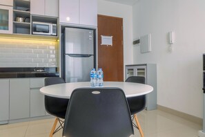 Eine moderne Küche mit Kühlschrank, Mikrowelle und Wasserspender. Ein runder Tisch mit Stühlen und eine Holztür sind im Hintergrund zu sehen.