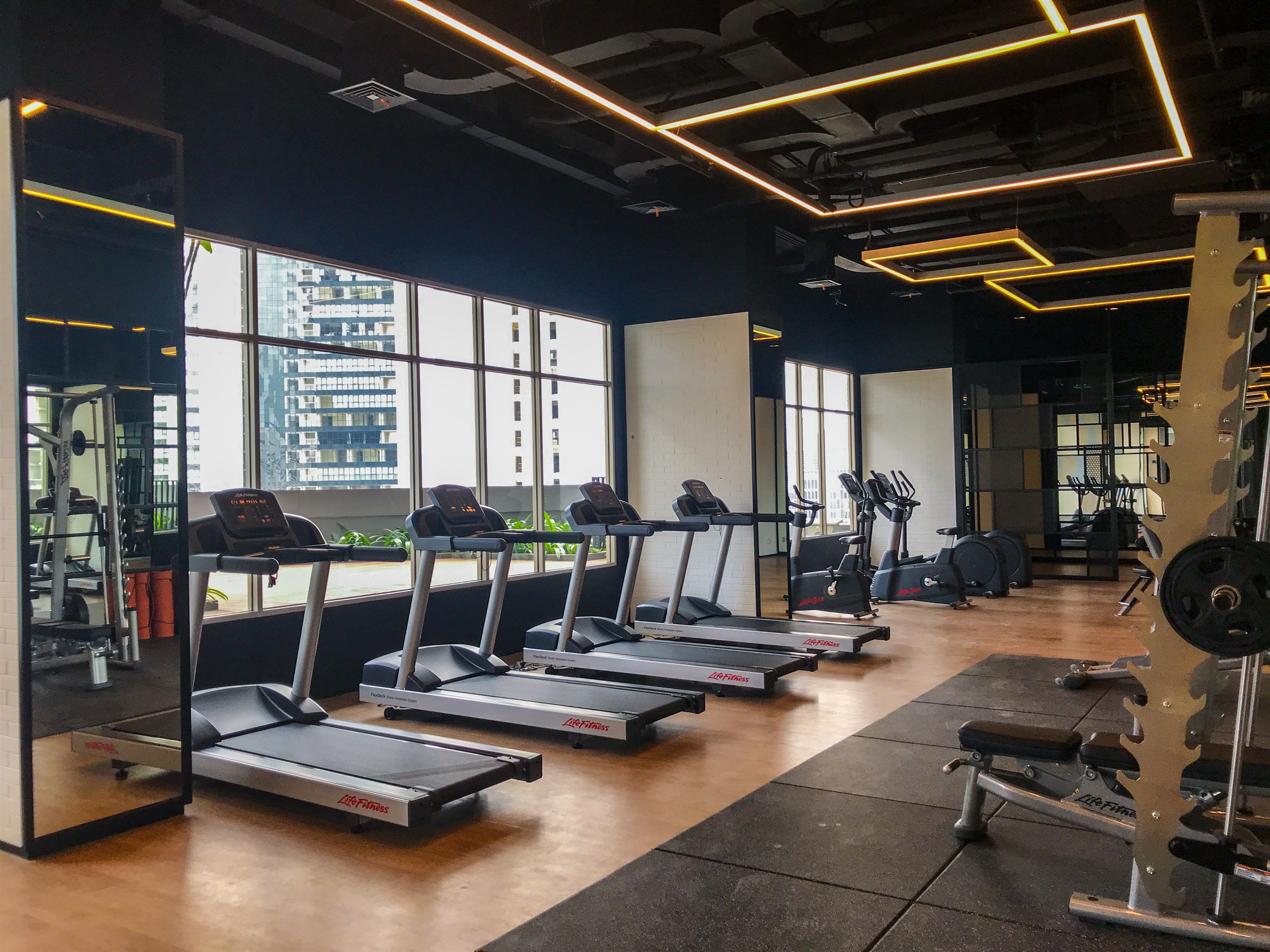 Una palestra con tapis roulant, macchinari per pesi e ampie finestre che offrono vista sugli edifici.