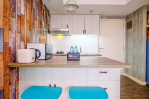 Cozinha compacta com painéis de parede em madeira, micro-ondas, chaleira e dispensador de água no balcão.